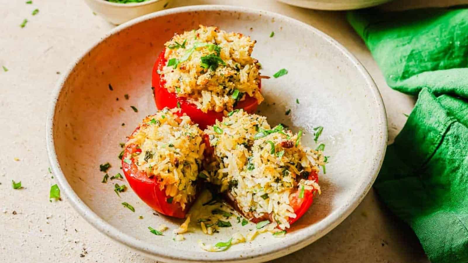 Three stuffed tomatoes filled with rice and herbs are served in a beige bowl, garnished with chopped parsley.