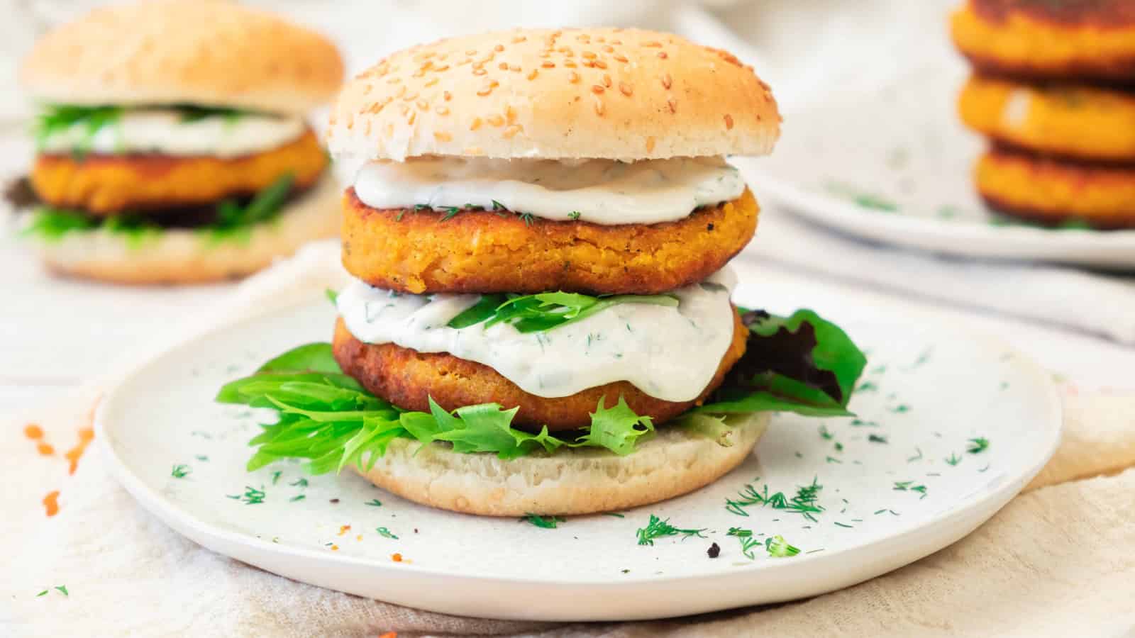 A veggie burger with lettuce, sauce, and two patties on a sesame bun, served on a white plate.
