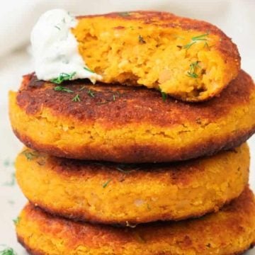 Three sweet potato patties stacked on a plate, topped with a dollop of sauce and a sprinkle of herbs.