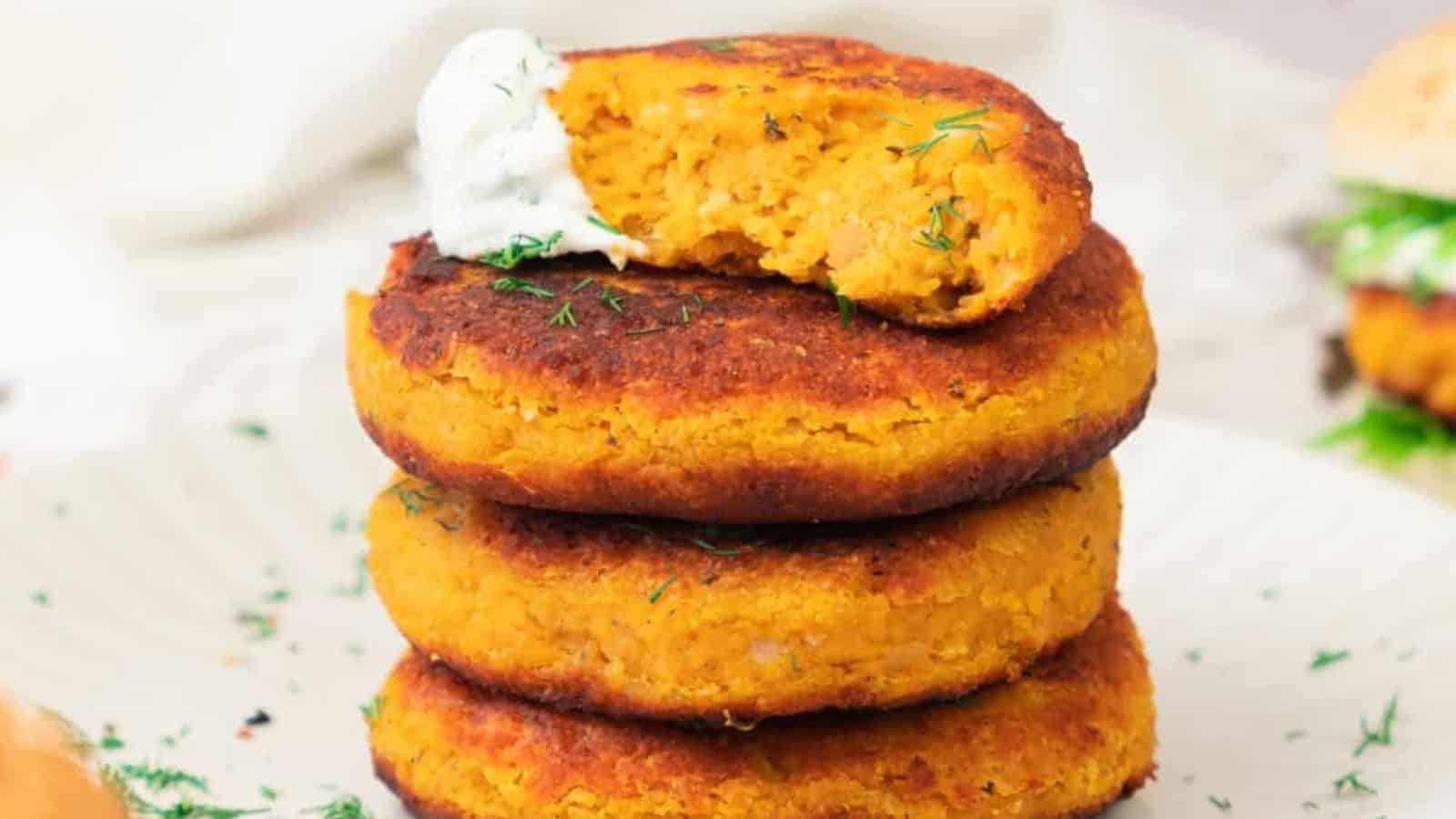 Three sweet potato patties stacked on a plate, topped with a dollop of sauce and a sprinkle of herbs.