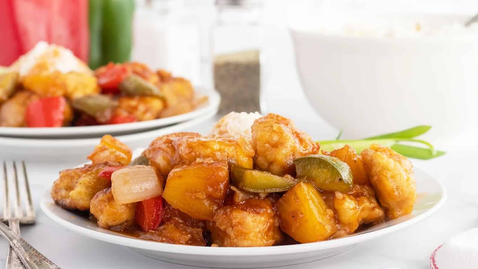 Plate of sweet and sour chicken with pineapple, bell peppers, onions, and rice on a white table.
