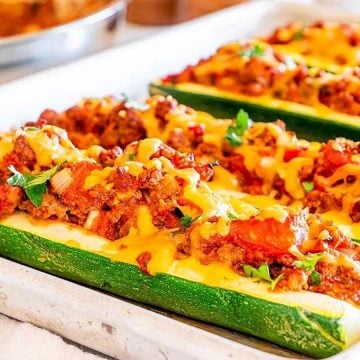 Zucchini boats filled with ground meat, tomatoes, and melted cheese, garnished with herbs on a baking sheet.