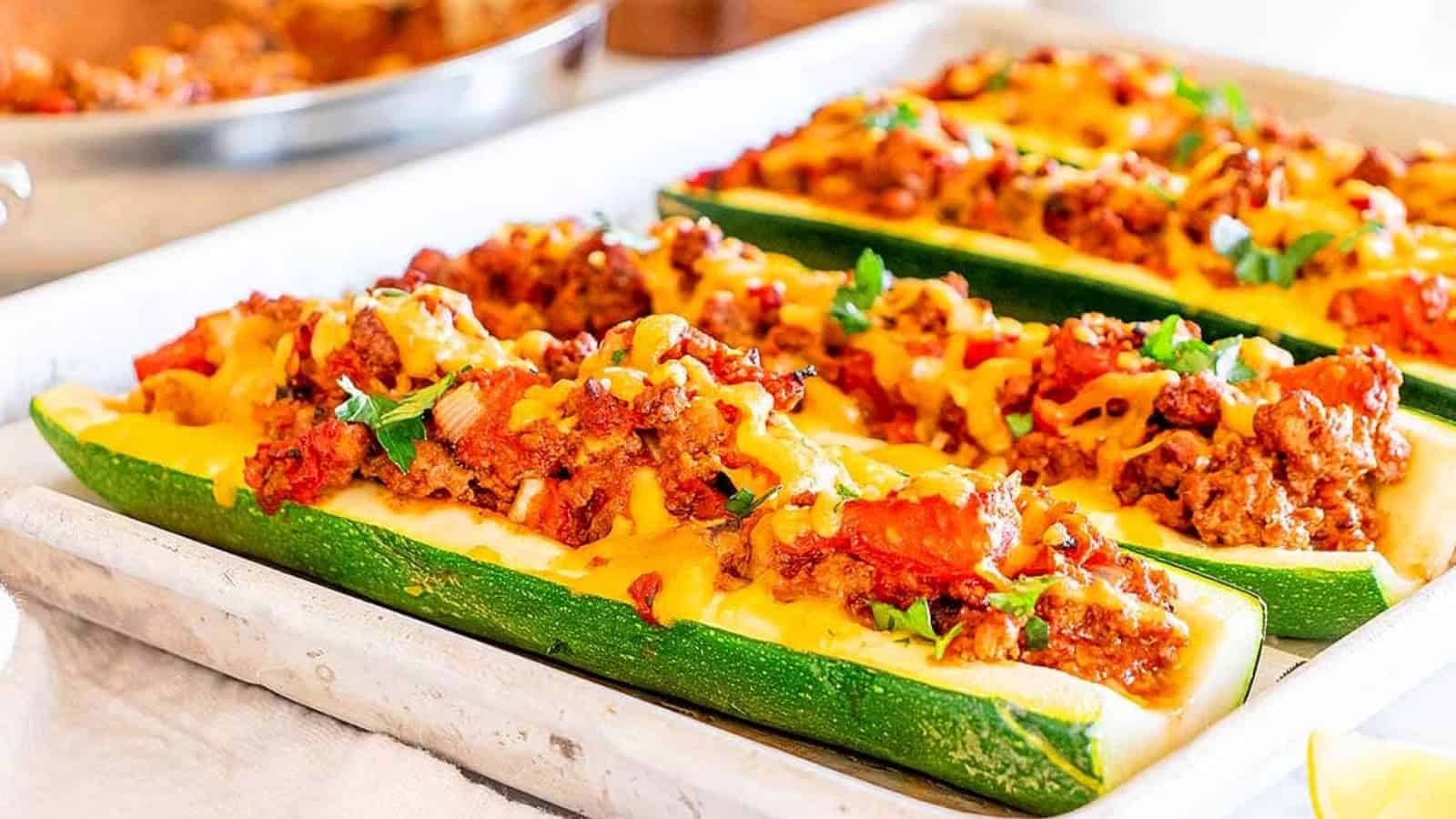 Zucchini boats filled with ground meat, tomatoes, and melted cheese, garnished with herbs on a baking sheet.