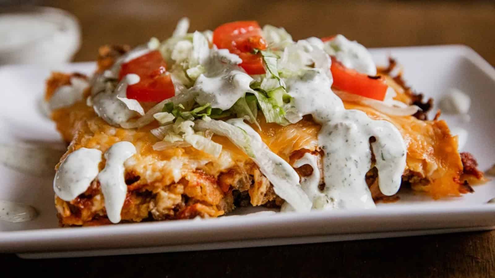 A cheesy casserole inspired by Global Ground Beef Dinners, topped with lettuce, tomatoes, and ranch dressing on a white plate.