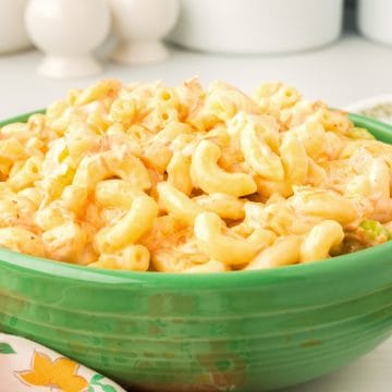 A green bowl filled with creamy macaroni and cheese sits on a table beside a floral napkin.