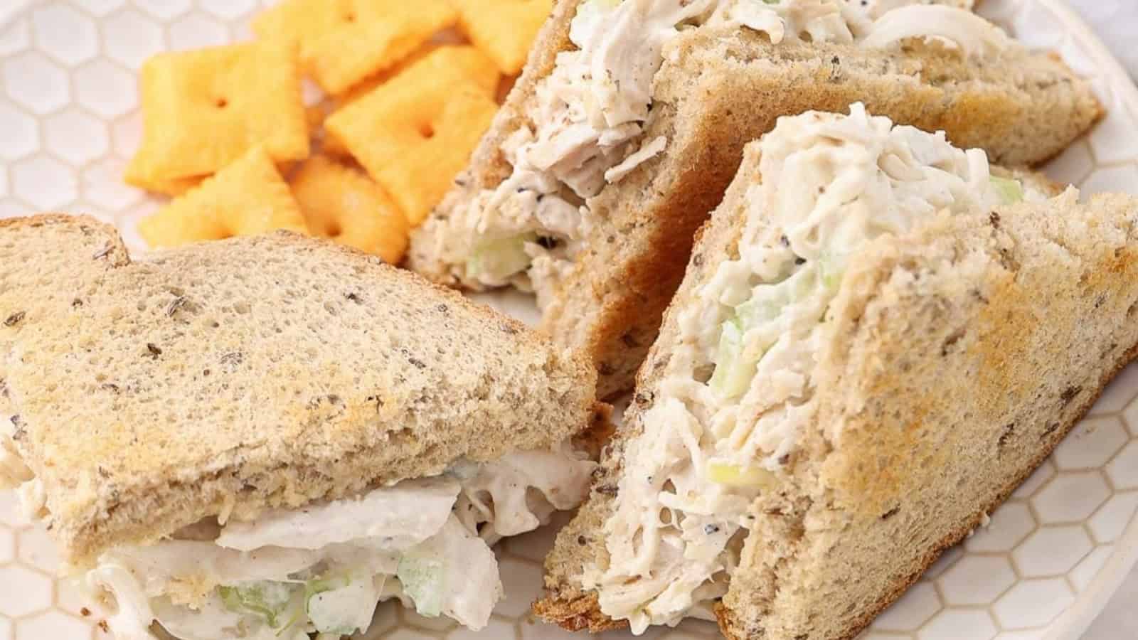 Chicken salad sandwich on wheat bread, served with cheese crackers on a white plate.