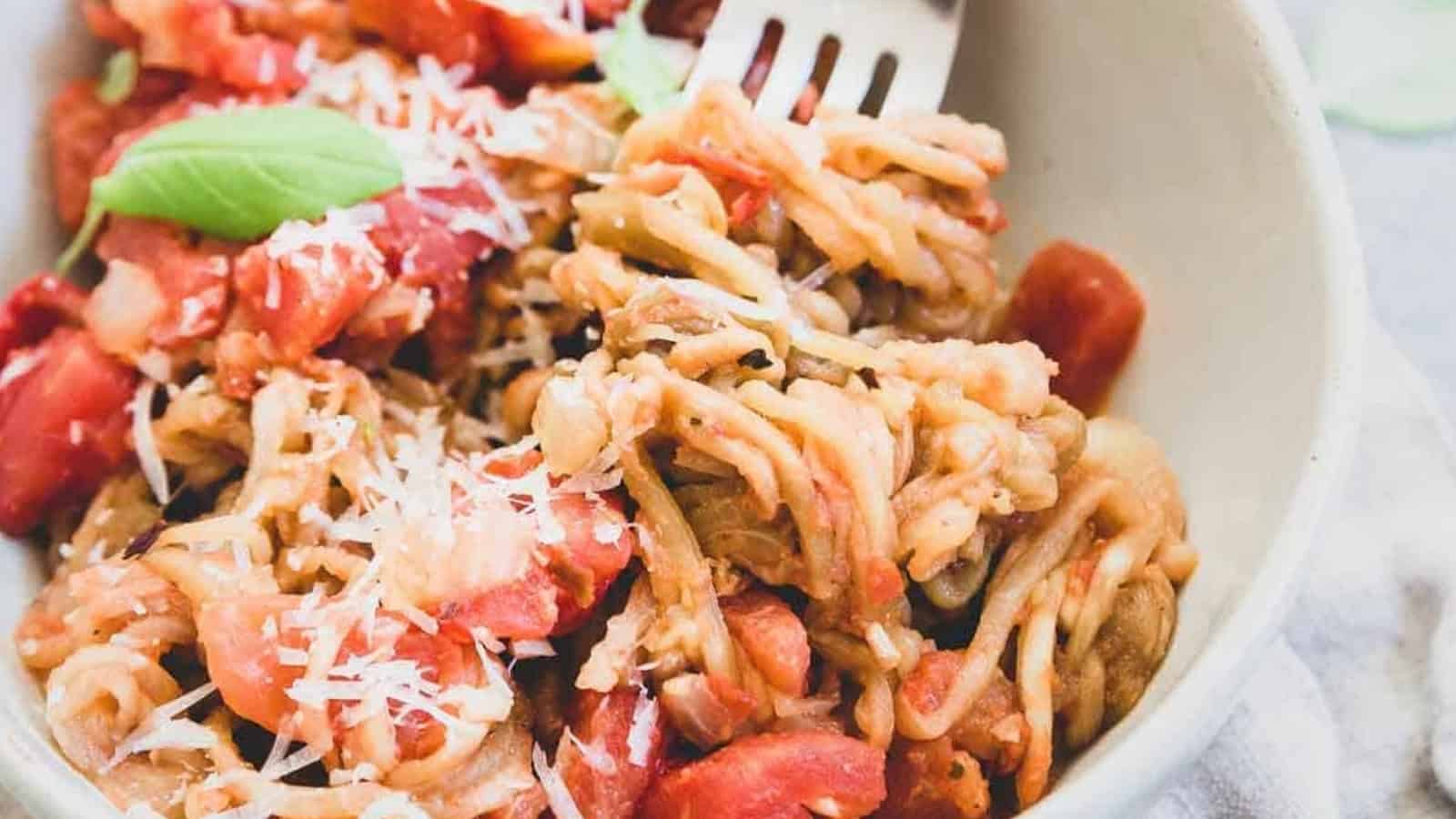 A bowl of spaghetti with tomato sauce, grated cheese, and a basil leaf, with a fork twirling the pasta.