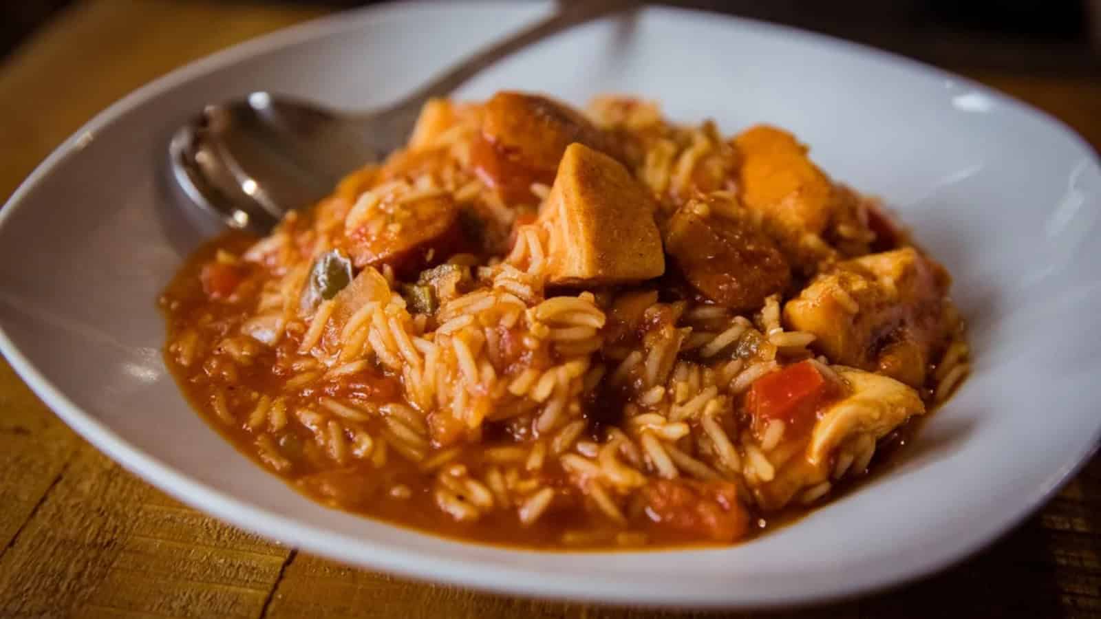 A plate of jambalaya with rice, chicken, sausage, and vegetables, served with a spoon.