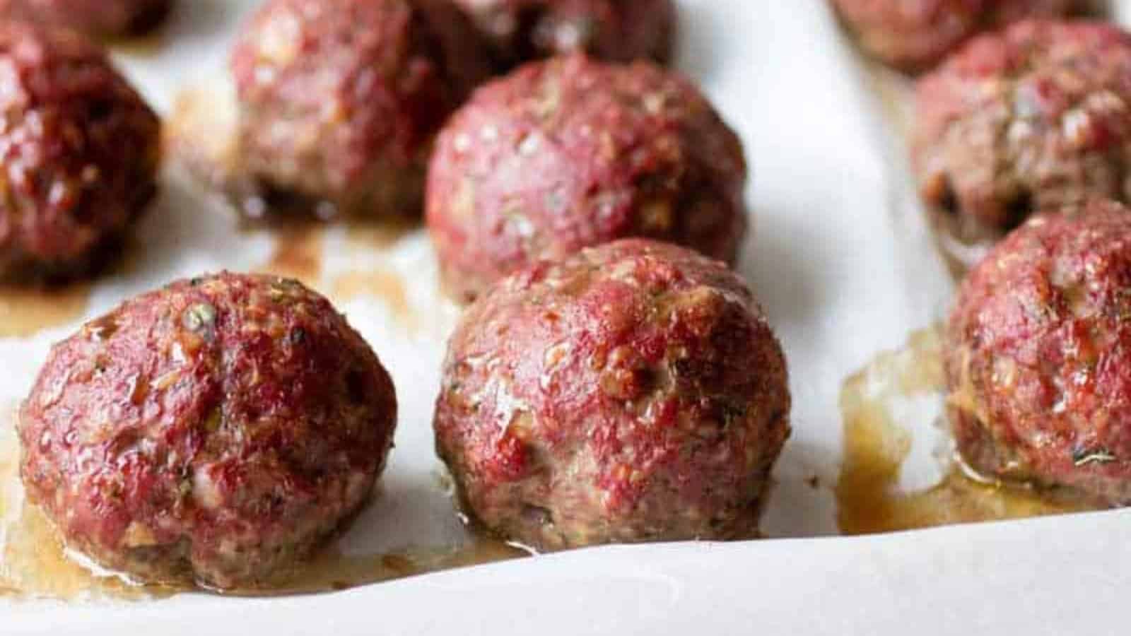 Close-up of freshly baked meatballs on a parchment-lined baking sheet.