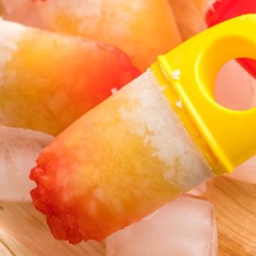 Colorful homemade popsicles with ice cubes on a wooden tray, featuring yellow and orange shades.