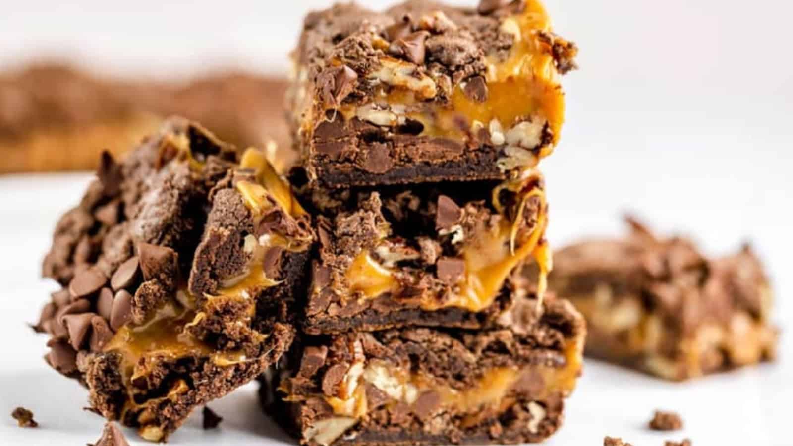 Stack of caramel brownies with chocolate chips and pecans on a white surface.