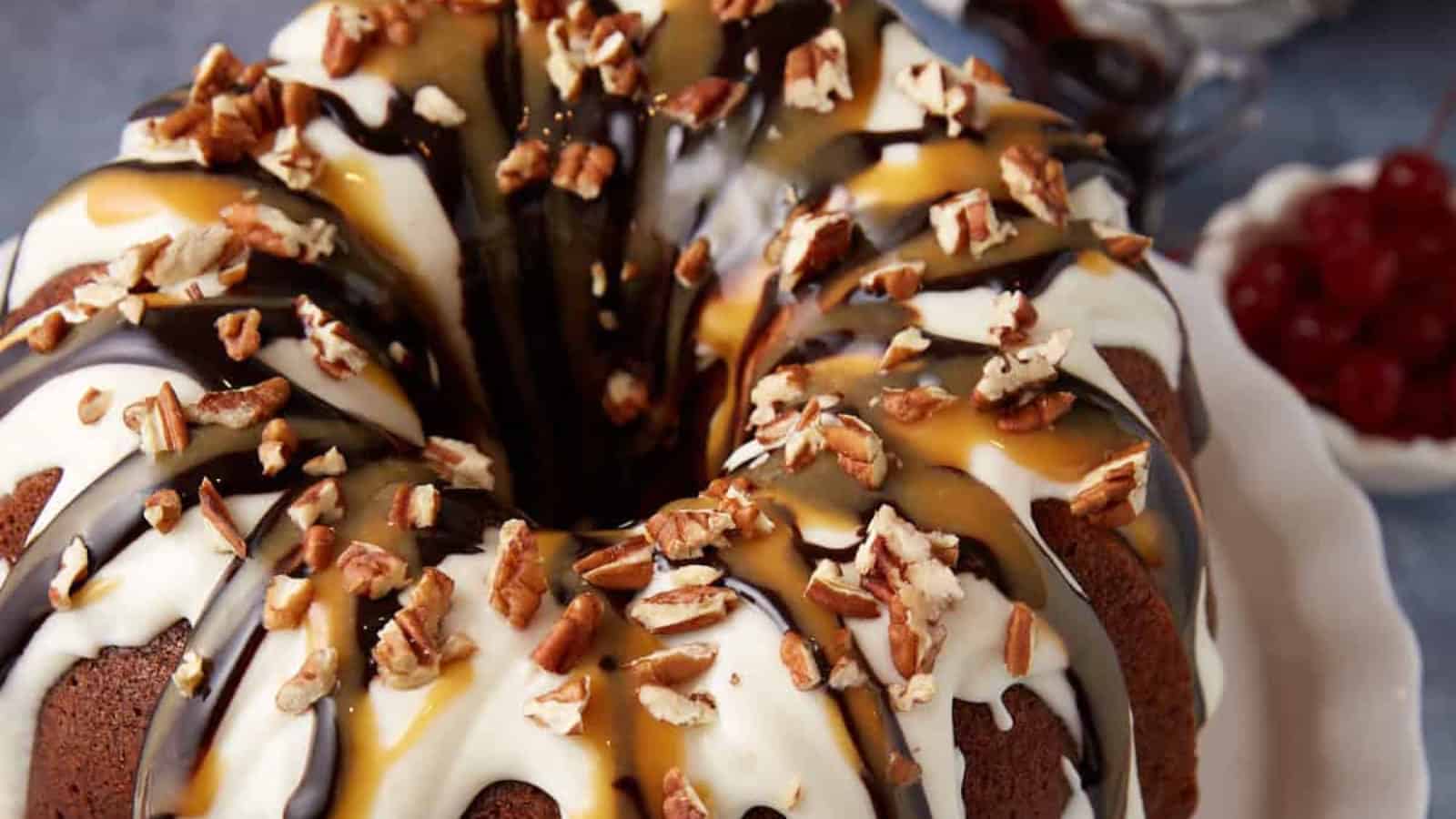 Bundt cake with white and dark chocolate glaze, caramel drizzle, and chopped pecans on top.