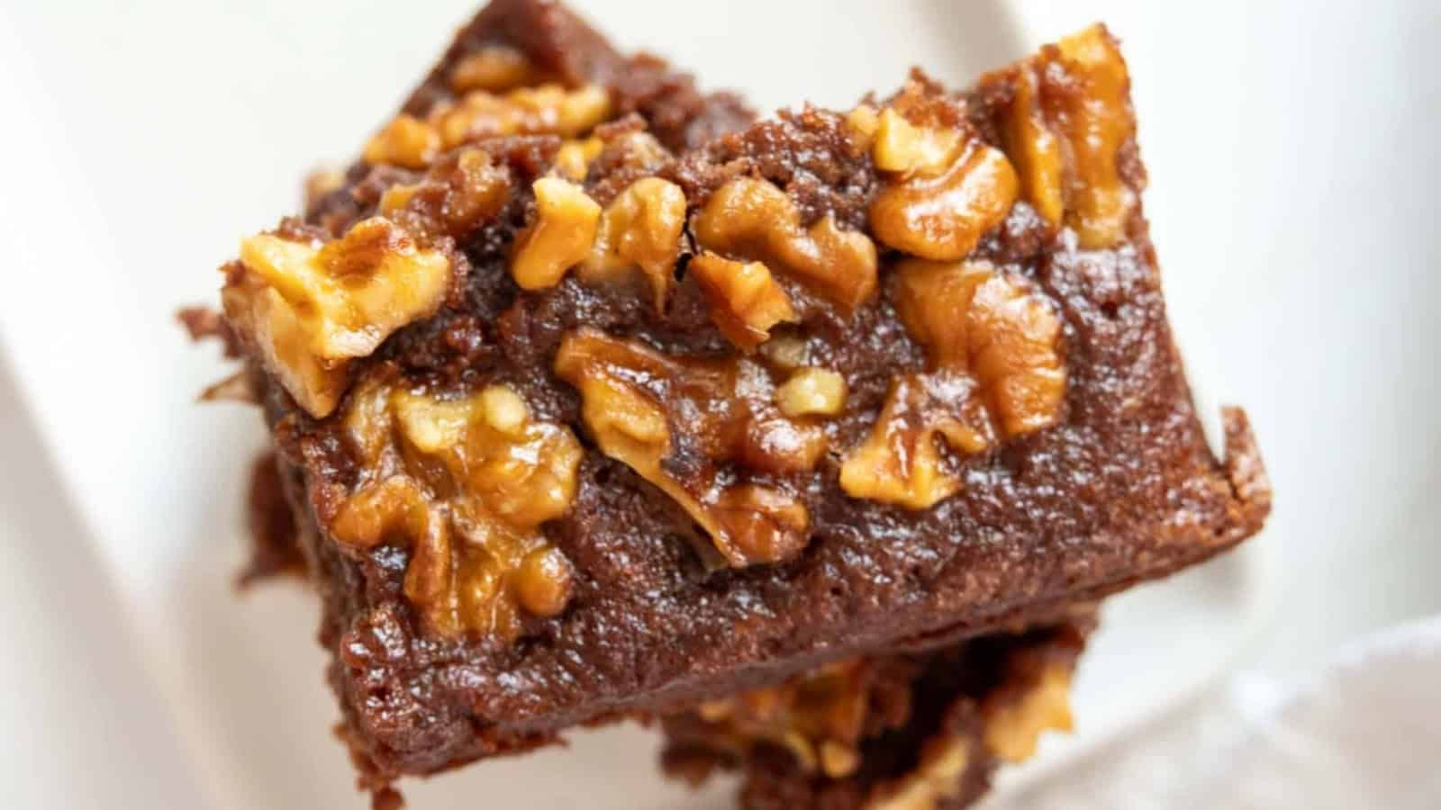 A close-up of a chocolate brownie topped with chopped walnuts on a white plate.