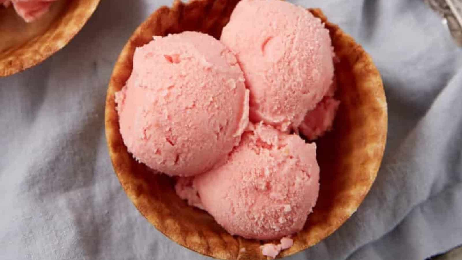 Three scoops of pink ice cream in a waffle bowl on a light blue cloth.