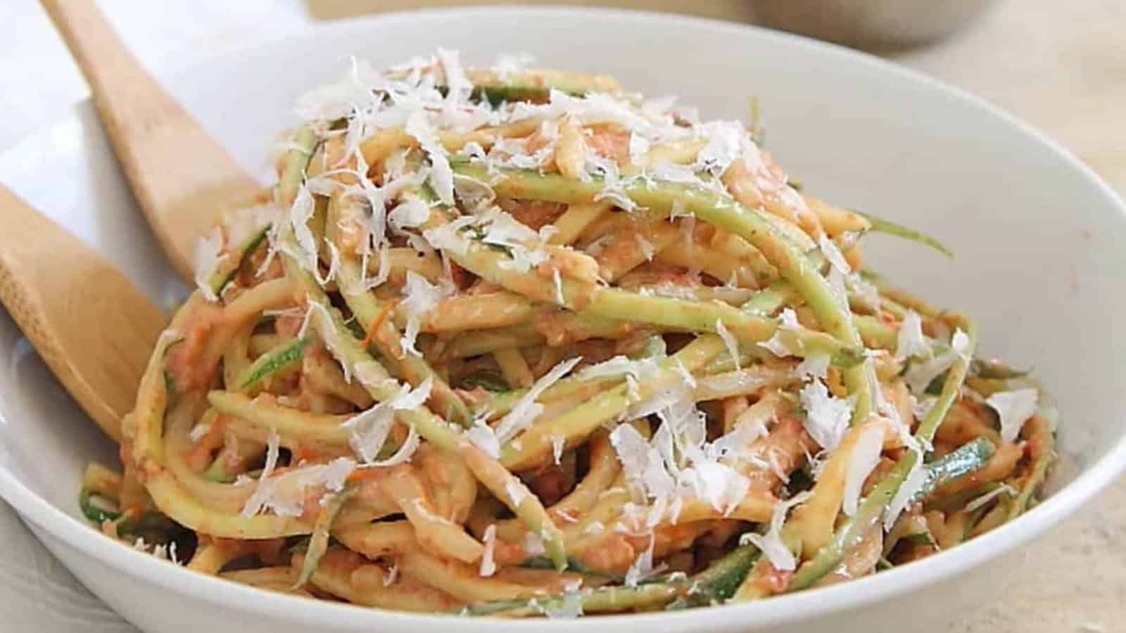 Zoodles with tomato sauce and grated cheese in a white bowl, with wooden utensils on the side.